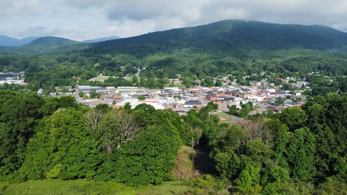 Town rooftops below a forested mountain ridge