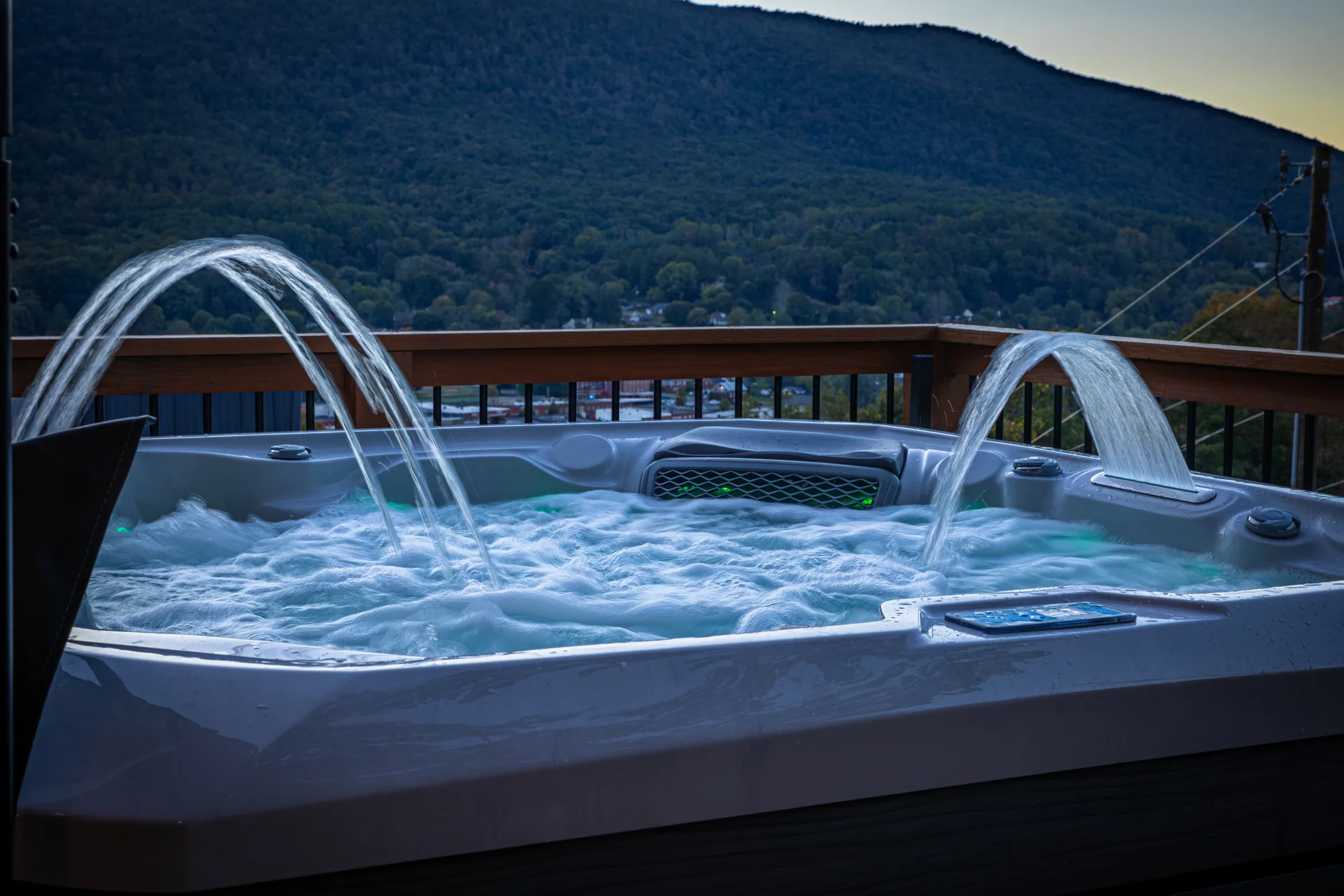 Hot tub with arcing water jets facing a green mountain at dusk at High Peak in West Jefferson, NC.