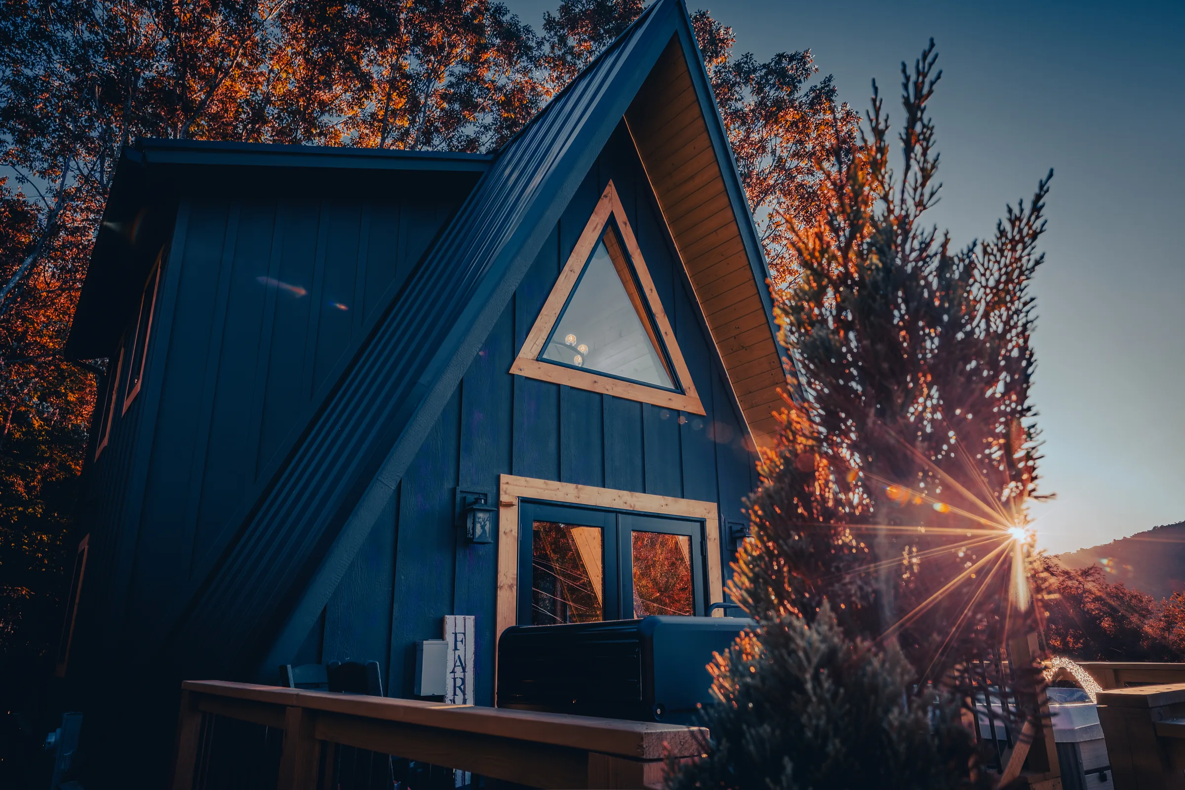 Sun setting through red leaves beside a High Peak A-frame in West Jefferson, NC.