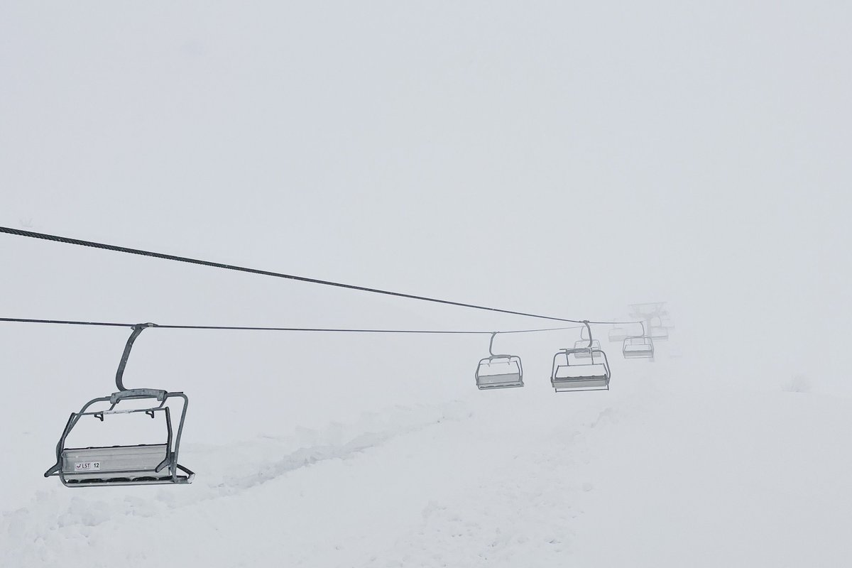 Empty ski chairlifts climbing into winter fog above a snowy slope.