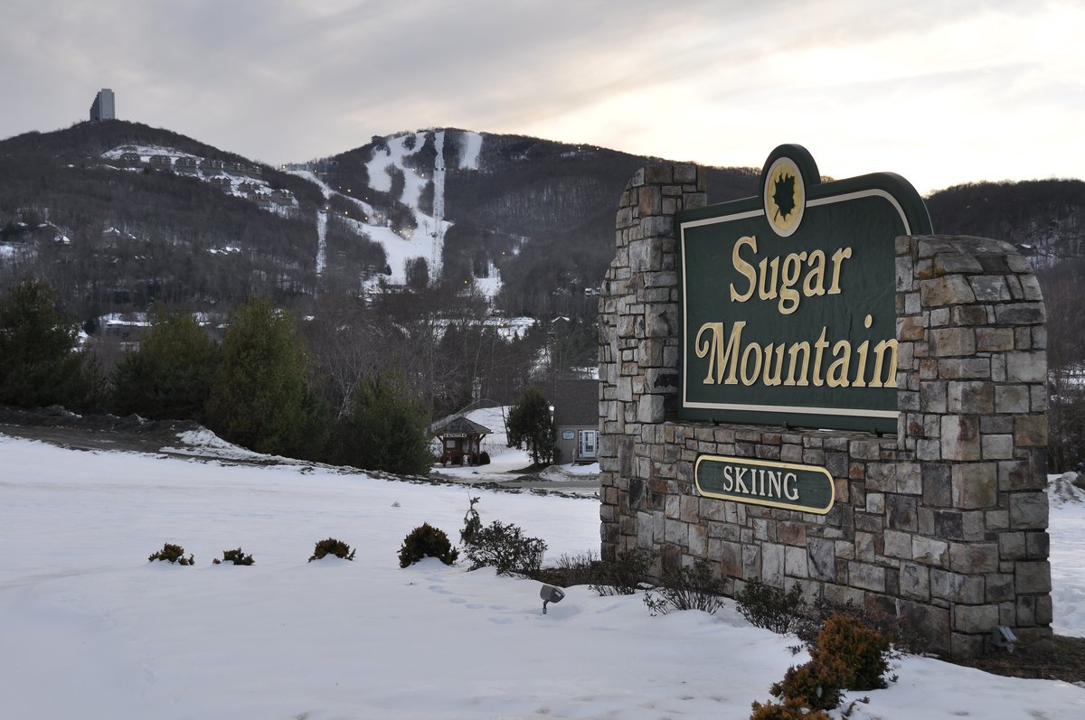 Stone Sugar Mountain Skiing sign in fresh snow with the ski slopes rising behind it.