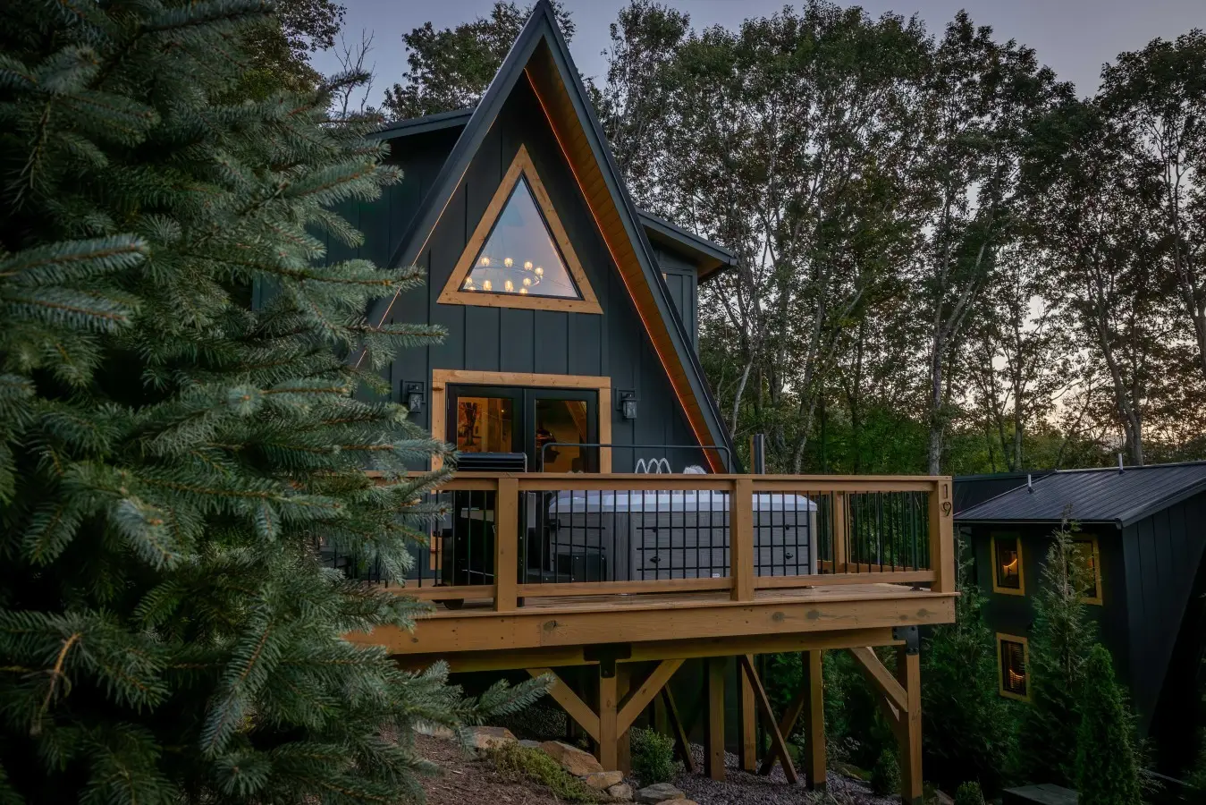 A-frame cabin with hot tub deck among the trees at dusk