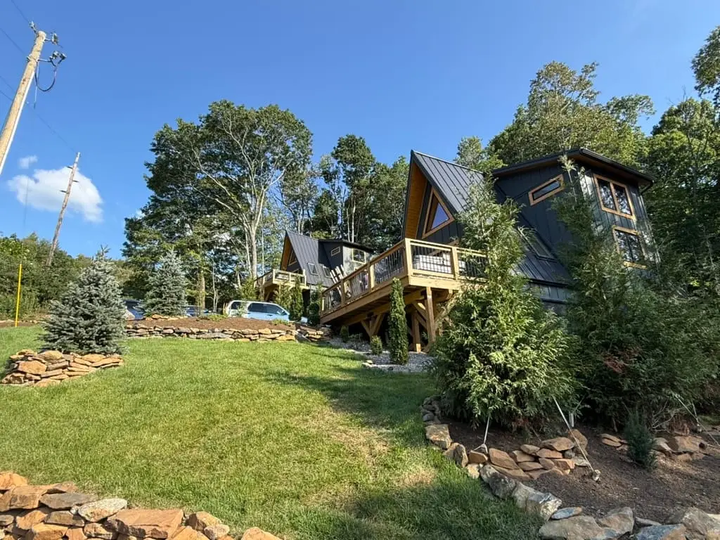 Two High Peak A-frame cabins with wood decks on a grassy slope in West Jefferson, NC